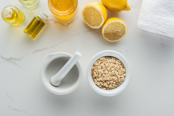 top view of bowl with oat flakes, pounder, lemons and various components for homemade cosmetics on white surface - Fotografie, Obrázek
