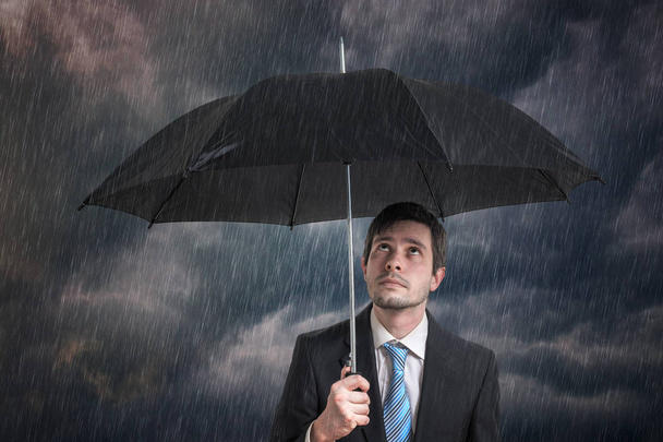 Pessimistischer Geschäftsmann mit schwarzem Regenschirm im Sturm. - Foto, Bild