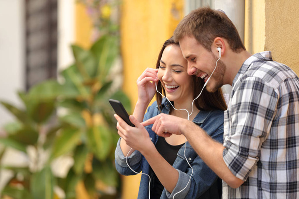 Portrait of a happy couple laughing listening to music online in the street - Foto, Imagem