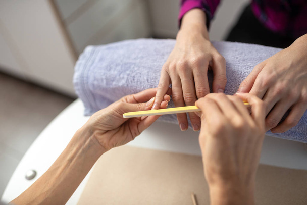 Over the shoulder view of professional manicurist filing nails of a woman in a manicure treatment. - Photo, Image