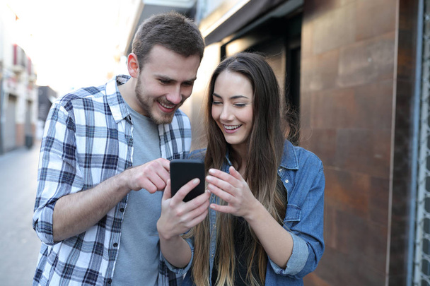 Two happy friends or couple using a smart phone walking in the street - Zdjęcie, obraz