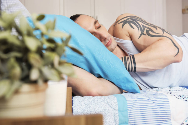 Jovem musculoso com tatuagens no ombro dormindo confortavelmente em seu travesseiro no quarto
 - Foto, Imagem