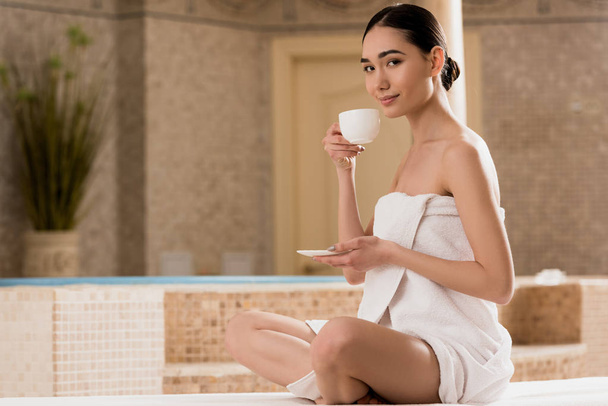 piękna kobieta w ręcznik, picia kawy i patrząc na kamery  - Zdjęcie, obraz
