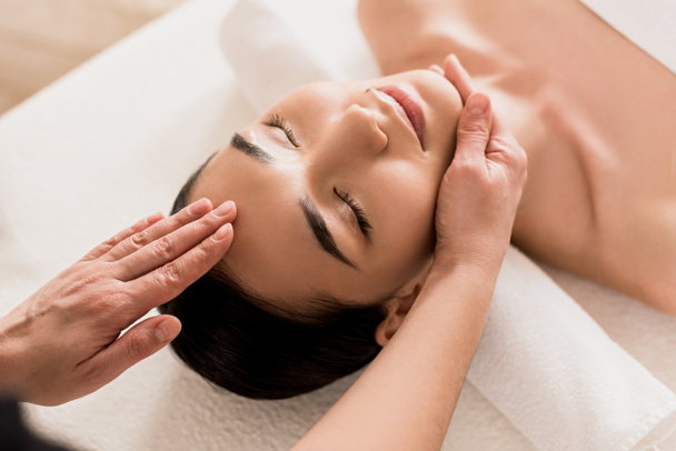 приваблива азіатська жінка отримує масаж обличчя з закритими очима в спа-центрі
  - Фото, зображення