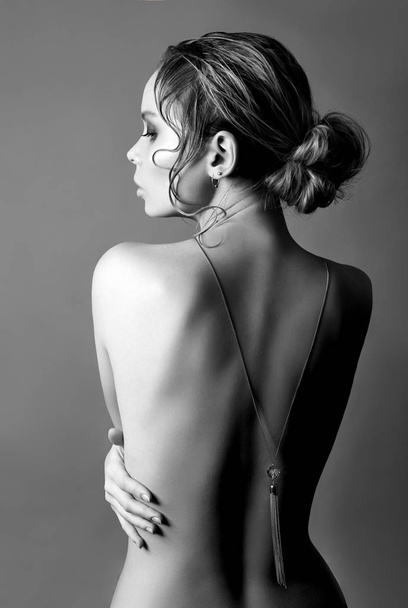 Art of Nude fashion Nude back blonde on grey background, pendant necklace on chain on back. Beauty and skin care perfect body. Girl hugs her hands - Foto, afbeelding