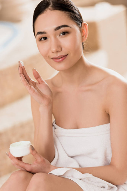 beautiful asian woman in towel applying cosmetic cream at spa  - Fotó, kép