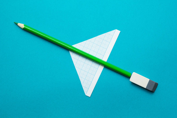 Green airplane made of pencils and paper on a blue background. Childish imagination. - Foto, Bild
