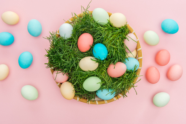 top view of easter eggs in wicker plate with grass isolated on pink - Foto, Bild
