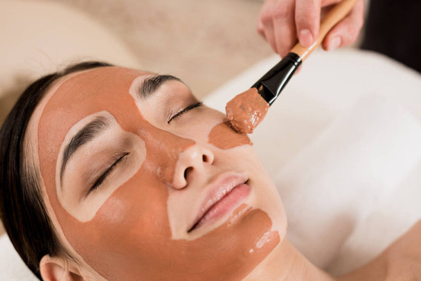 abgeschnittene Ansicht der Kosmetikerin Anwendung Maske auf schöne Frau Gesicht - Foto, Bild