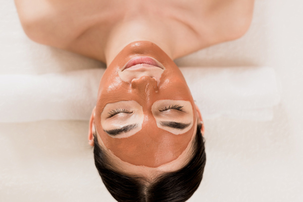 beautiful woman lying with clay mask on face at spa  - Φωτογραφία, εικόνα