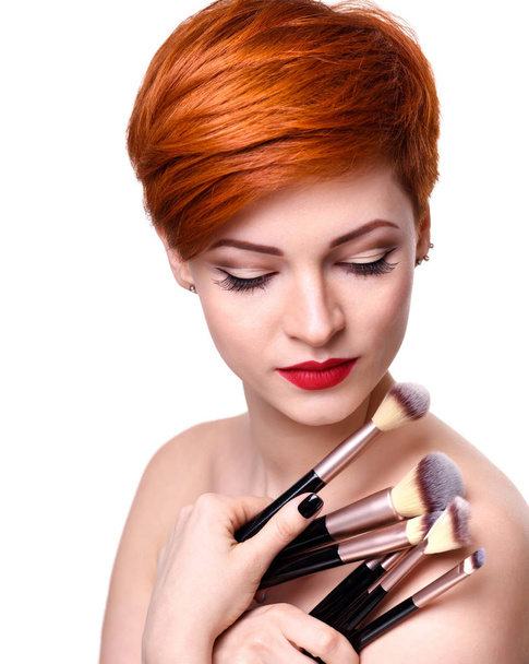 Portret van een mooie jonge vrouw met kort rood haar met make-up borstels - Foto, afbeelding
