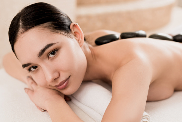 bela mulher recebendo pedra massagem e olhando para a câmera no spa
  - Foto, Imagem