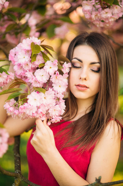 Porträt eines hübschen Mädchens im Sakura-Baum. Sakura-Blumen umgeben das Mädchen. Sakura-Ast neben ihrem Gesicht - Foto, Bild
