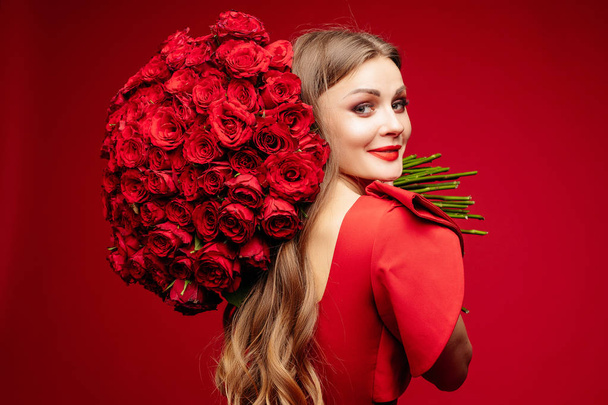 Beautiful young brunette lady in red with bunch of red roses on shoulder. - Fotografie, Obrázek