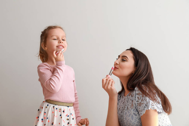 Porträt des niedlichen kleinen Mädchens und der Mutter mit Lippenstiften auf hellem Hintergrund - Foto, Bild