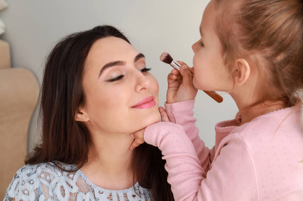 Linda hijita aplicando maquillaje en la cara de la madre
 - Foto, Imagen