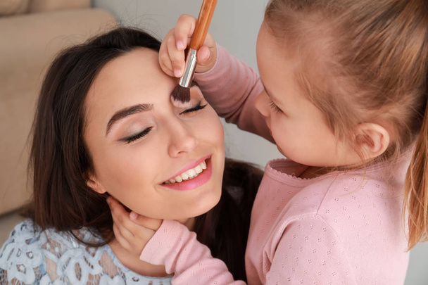 Cute little daughter applying makeup onto mother's face - Fotoğraf, Görsel