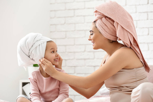 Cute little daughter with her mother after shower sitting on bed - Photo, Image