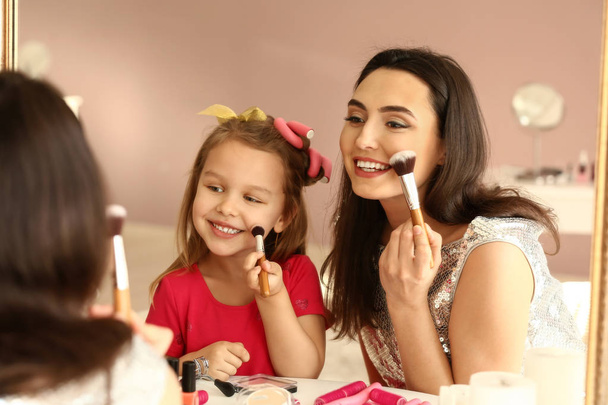 Cute little daughter and her mother doing makeup at home - Foto, afbeelding