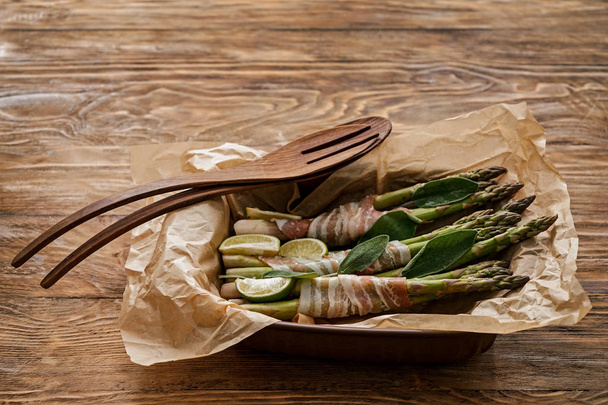 Baking dish with bacon wrapped asparagus on wooden table - Photo, Image