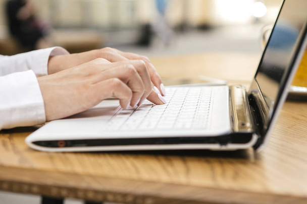 Mujer escribiendo en un teclado portátil en un cálido día soleado al aire libre, sentado en la mesa de la cafetería. Espacio para texto
. - Foto, Imagen
