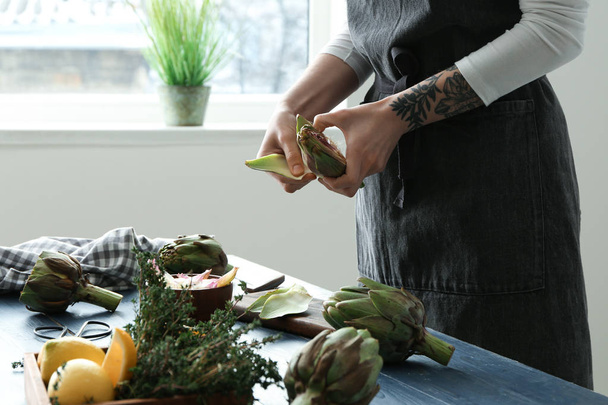 Woman preparing tasty raw artichokes in kitchen - Fotó, kép