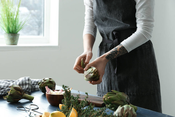 Woman preparing tasty raw artichokes in kitchen - Fotó, kép