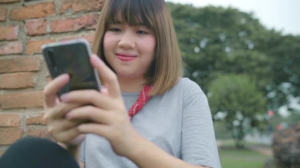 Reisende asiatische Frau, die mit dem Smartphone soziale Medien checkt, während sie sich entspannen, nachdem sie ihre Urlaubsreise in Ayutthaya, Thailand, verbracht hat, genießen Frauen ihre Reise an erstaunlichen Sehenswürdigkeiten in der traditionellen Stadt.  - Filmmaterial, Video