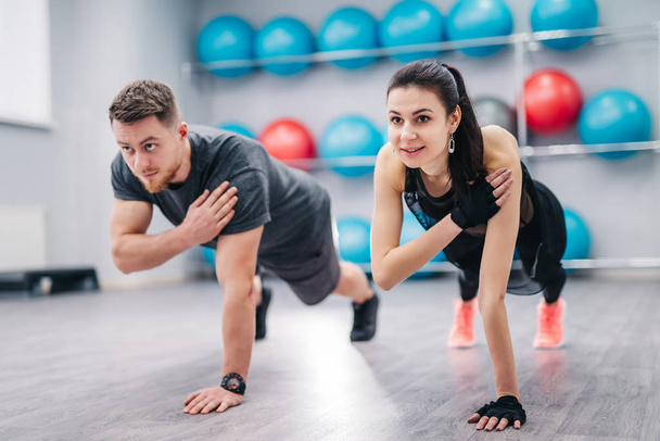 Beautiful woman and strong male doing push-ups on one hand with a background of fitness balls. Young couple is working out at gym - Valokuva, kuva