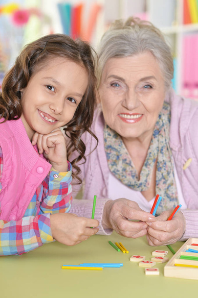 grandmother with granddaughter counting with sticks while sitting at table in room - Foto, Imagen