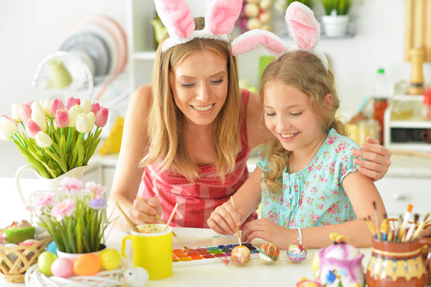  Mother with daughter wearing rabbit ears decorating  Easter eggs at home  - Photo, image