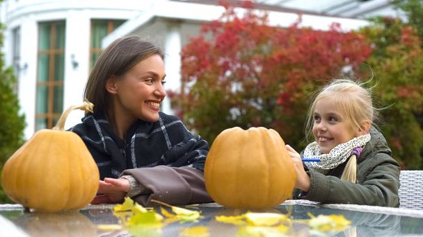 Cheerful girl and mom painting scary face on pumpkin, spend time together, fun - 写真・画像