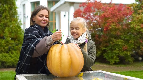 Mother and daughter carving pumpkin jack-o-lantern, having fun together, weekend - 写真・画像