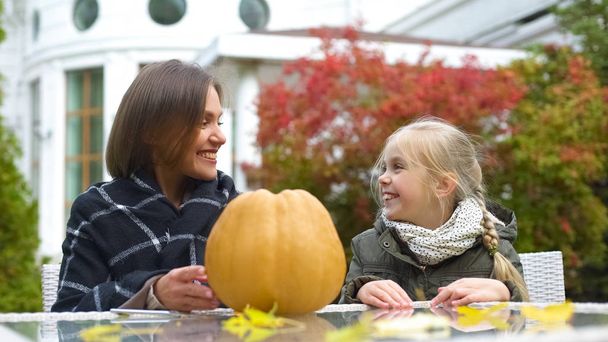 Mom and girl preparing pumpkin for party, sitting on backyard, happy moments - 写真・画像