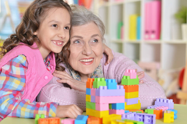 Cute girl and grandmother playing with colorful plastic blocks  - Фото, изображение