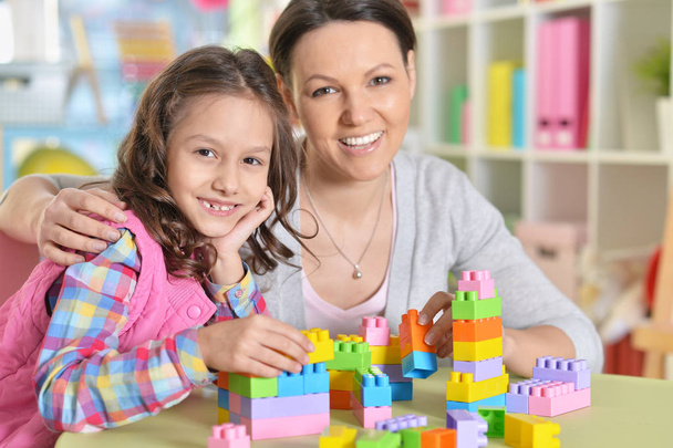 Curly little girl and her mother playing with colorful plastic blocks at home - Фото, изображение