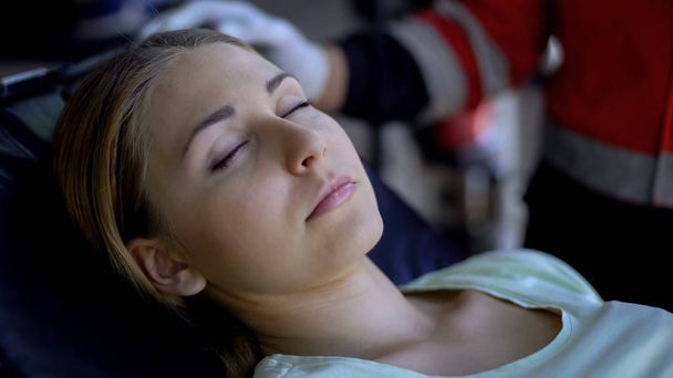 Mujer pálida yaciendo inconsciente en camilla primer plano, paramédico proporcionando primeros auxilios
 - Foto, imagen