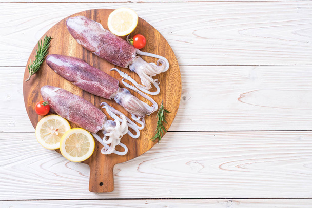 fresh octopus or squids raw on wooden board with ingredients - Foto, afbeelding