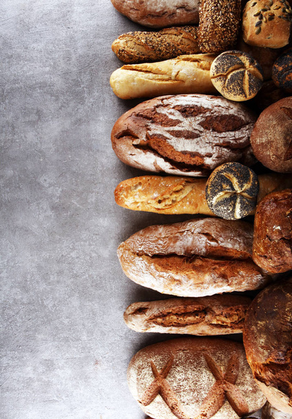 Sortiment aus gebackenem Brot und Brötchen auf Steintischhintergrund. Bäckerplakat-Konzept - Foto, Bild