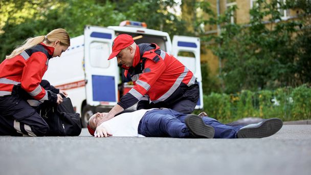 Doctors providing urgent care to unconscious man, heart attack or car accident - Fotó, kép