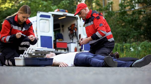 Paramedics helping unconscious man on road, making injection with insulin - Fotó, kép