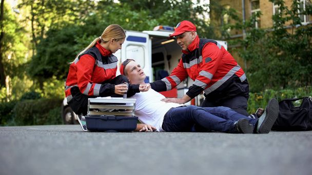 Ambulance medic giving painkiller to man lying on road, qualified emergency care - Foto, afbeelding