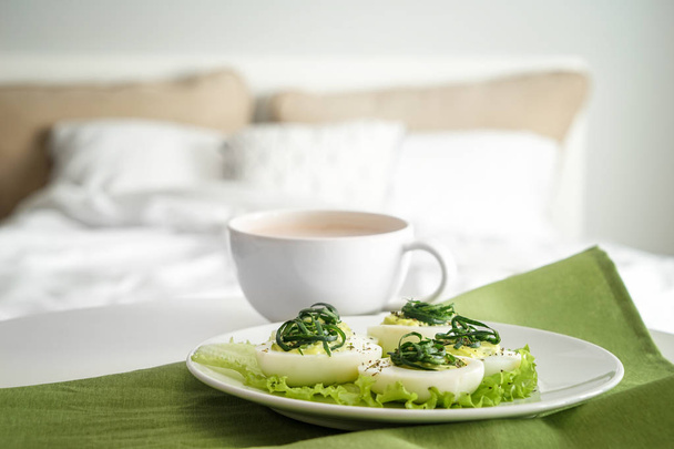 Plate with tasty deviled eggs and cup of coffee on bed - Photo, Image