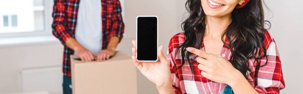 vista ritagliata di donna felice che punta con il dito allo smartphone con schermo bianco vicino all'uomo a casa
 - Foto, immagini