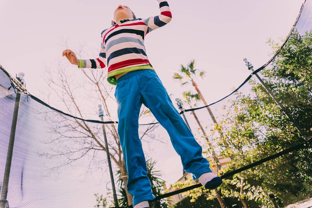 5 year old boy jumping on a trampoline exercising in the backyard of his house, enjoying the spring with gesture of happiness and lifestyle. - Fotografie, Obrázek
