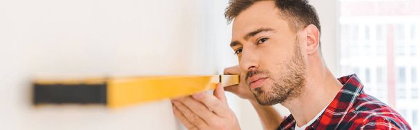 serious man measuring wall at home - Фото, изображение