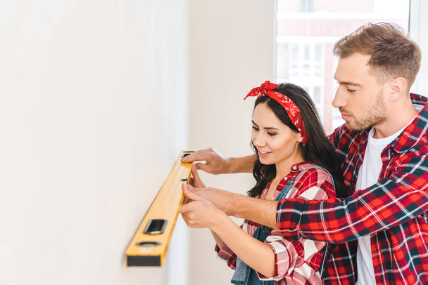 cheerful couple holding measuring level near wall at home - 写真・画像