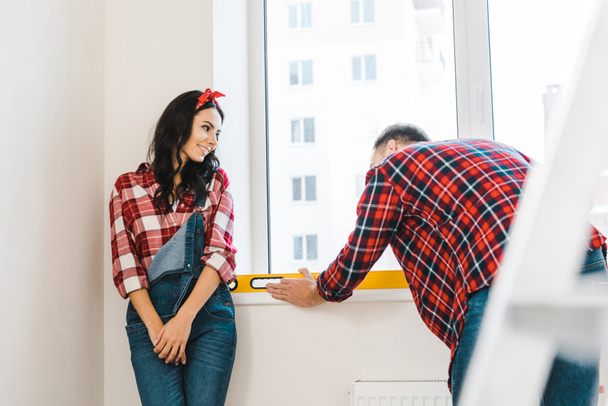 cheerful woman looking at boyfriend measuring heating radiator - Fotografie, Obrázek