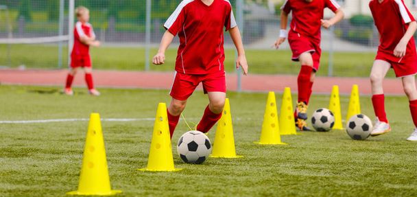 Soccer camp for kids. Boys practice dribbling in a field. Players develop good soccer dribbling skills. Children training with balls and cones. Soccer slalom drills to improve football dribbling pace - Foto, Imagem
