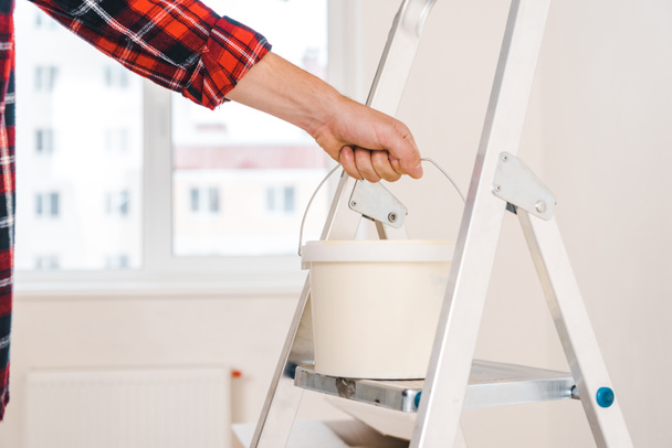 cropped view of man holding paint bucket in hand on ladder  - Foto, afbeelding